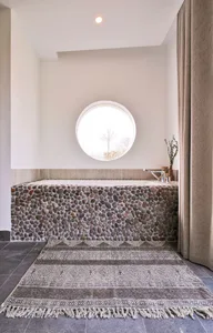 A modern bathroom with a granite-tiled surround, a freestanding bathtub, and a round window letting in natural light.