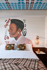 An industrial-style bedroom featuring a wall mural of a person with a stylish haircut and a textured ceiling.