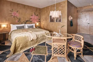 A luxurious bedroom with metallic fabric bedding, gold accents, and a stylish chair with a glass table.