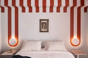 A modern bedroom with a striped ceiling, patterned bedding, and a framed abstract portrait on the wall.