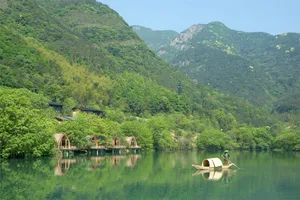 A serene waterfront resort with lush greenery, a boat, and mountains in the background.