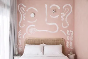 Pink wall with white paint strokes and symbols above the rattan headboard of a double bed.