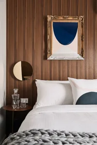 A modern bedroom with a wooden panel wall, white bedding, and a decorative bedspread.