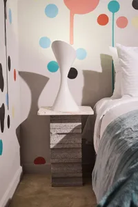 A modern bedroom featuring a stylish bedside table made of concrete and marble, with a unique vase on top.