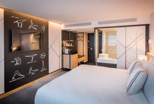 Modern minimalist hotel room with white bed, black accent wall, and open bathroom layout.