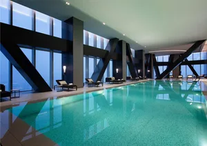 A modern indoor swimming pool with large glass walls and lounge chairs.