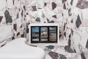 A retail franchise interior with a marble wall and floor, featuring a well-stocked beverage cooler.