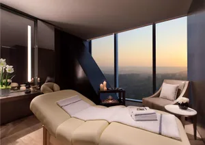 A modern spa room featuring a comfortable massage table with white towels and candles, overlooking a cityscape during sunset.