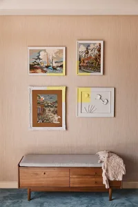 Four vintage framed prints on a beige textured wall with a wooden bench below them.