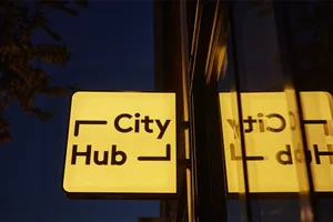 A glowing City Hub signage attached to a glass window at night.