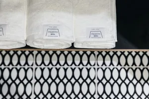 Three white towels with 'PEANUTS HOTEL' labels rolled up and placed on a shelf above a wall with black and white patterned ti