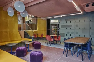 A modern cafe with yellow seating, blue chairs, purple poufs, and a vending machine.