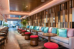 Contemporary lounge area of a hotel with wooden structures, fabric seating, and colorful throw pillows.
