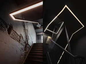 Modern, industrial-style staircase with black metal railing illuminated by linear, geometric lighting fixtures against a blac