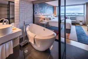 Modern minimalist bathroom with white marble finishes, floor-to-ceiling windows, and a freestanding bathtub.