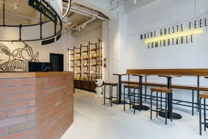 A modern restaurant cafe interior with brick and concrete finishes, featuring seating areas, a bar, and decorative elements.
