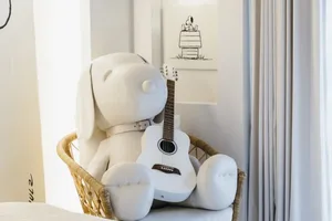 A white stuffed dog holding a white guitar on a white cushion.