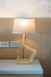 A wooden adjustable table lamp with a beige lampshade on a wooden surface.