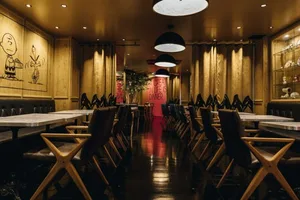 A dimly lit cafe interior with dark wooden tables and chairs, white walls, and red signage.