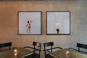 A modern cafe interior with concrete walls and wooden tables, featuring two framed artworks.