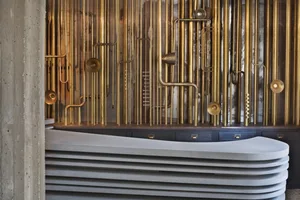 A modern reception desk featuring gold-colored metal pipes and a curved, stacked concrete top.