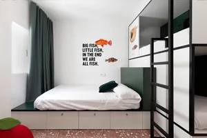 A minimalist bedroom featuring a white bed with green accents, green curtains, and a wall quote about fish.