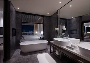 A modern bathroom with marble countertops, black granite walls, and a freestanding bathtub overlooking a cityscape.