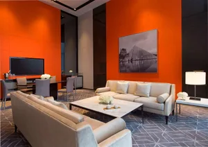 Modern minimalist lounge area with white sofas, marble coffee table, and orange accent wall featuring a black and white photo