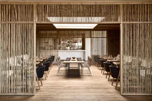A modern restaurant with wooden interiors, featuring tables, chairs, and a bar.