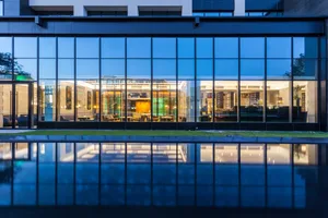 A modern hotel lobby featuring large glass windows reflecting the interior and a glossy floor.
