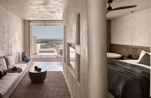 A minimalist bedroom with concrete walls, a large bed, and a view of the ocean through the windows.