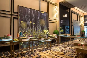 A spacious, elegant room with a forest-themed mural and various tables displaying decorative elements for an event.