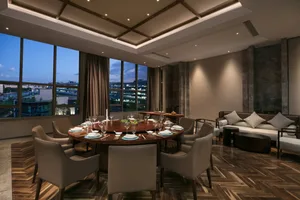 A modern residential dining room with a round wooden table, leather chairs, and large windows overlooking a cityscape.