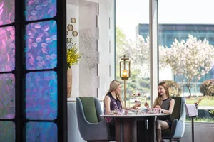 Two women enjoying a meal at a round table in a modern restaurant with glass walls and marble interior.