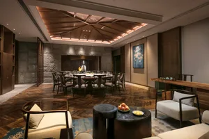 A cozy hospitality interior featuring wooden furniture and a stone wall with a round table and chairs in the center, illumina