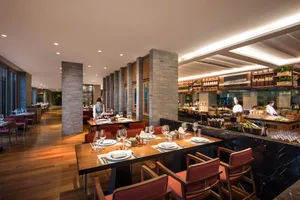 Modern restaurant interior with marble tables and chairs, stone flooring, and open kitchen counter.