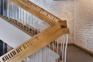 A modern industrial staircase constructed of wood with wooden brackets engraved with the phrase 'Killed by a Lover'.