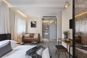 Modern minimalist bedroom with concrete floor, white walls, and a bed with white linens and gray throw blanket.
