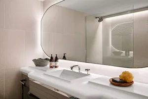 A sleek, minimalist bathroom with a white ceramic sink, glass shower enclosure, and polished surfaces.