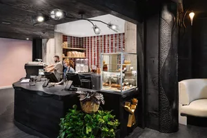 Industrial-style cafe interior with concrete wall, wooden counter, and green plants.