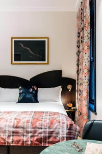 A mid-century modern bedroom with a bed featuring a plaid blanket, white pillows, and wooden headboard, patterned curtains, a