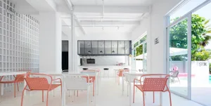 A minimalist cafe interior with white walls, pink chairs, and a bar counter