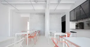 A minimalist cafe interior with white tables and chairs, white walls, and a white grid wall.