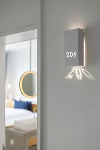 A minimalist hotel room with a grey cube-shaped light fixture displaying the room number 206.