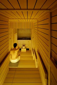A minimalist sauna with wooden walls and a person sitting on a mat inside.