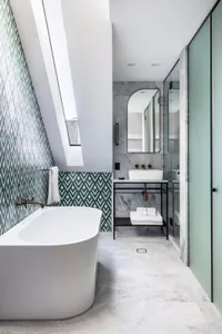 Modern bathroom featuring a freestanding bathtub, green and white patterned tiles, and a white countertop sink with a black m