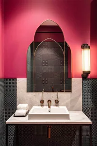 A modern bathroom with metallic mosaic tiles, an arched mirror, and a white sink on a marble countertop.