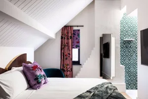 A modern bedroom featuring a neatly made bed with a floral-patterned pillow, a teal armchair, and a patterned green and white