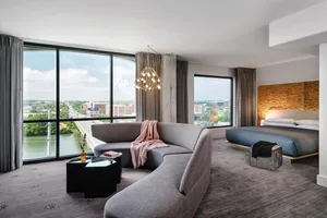Modern hotel room featuring a contemporary couch, bed, and large window overlooking a cityscape.