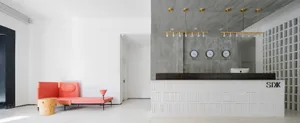 A modern lobby featuring a reception desk with clocks displaying time zones and a minimalist seating area with a pink couch a
